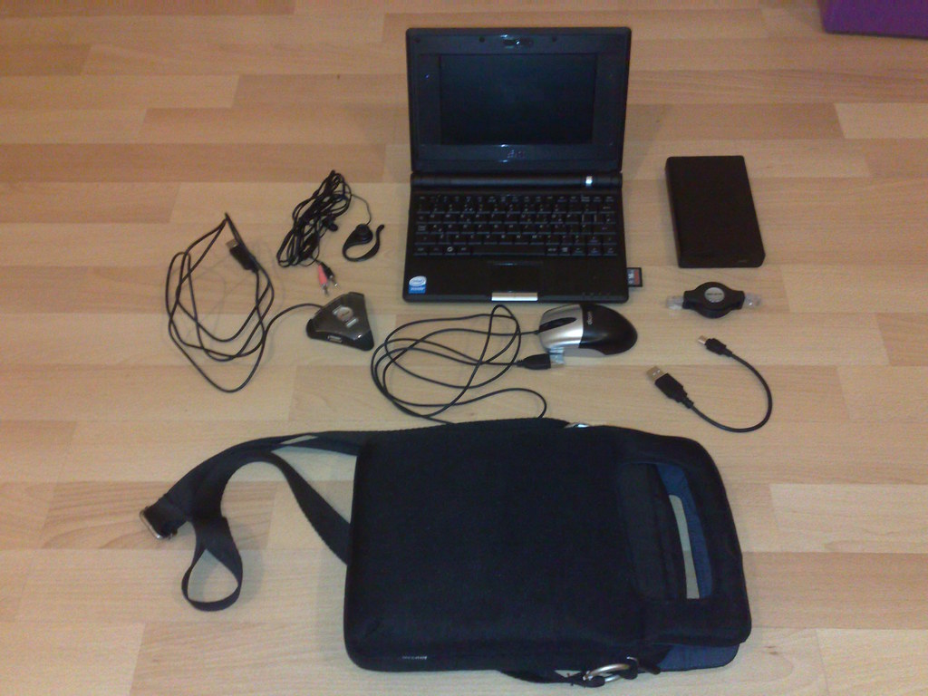 Laptop bag, small laptop, mouse, charger and cables laid out before a hybrid work day