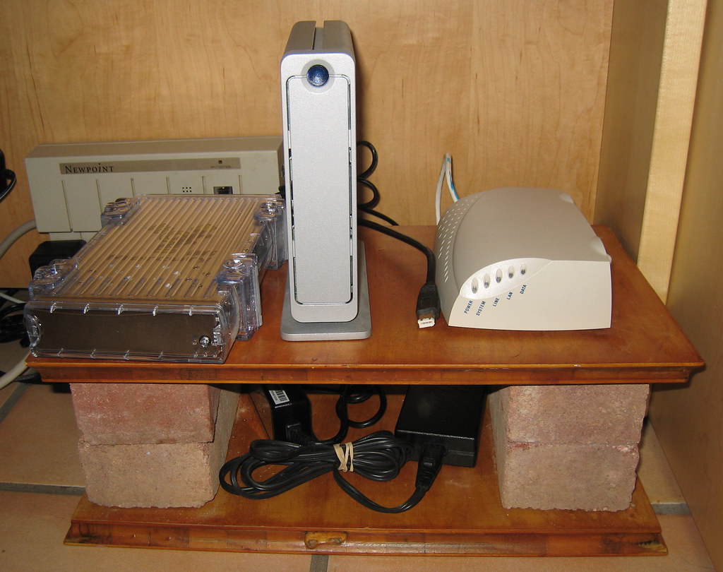 Small under-desk organizer shelf holding cables, adapters and network devices below a work surface